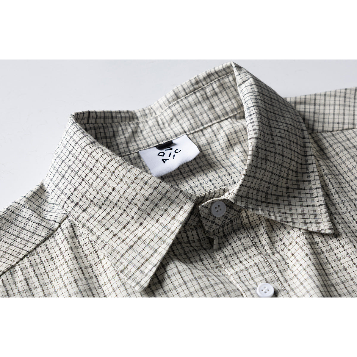 Close-up of a cream shirt with a fine black-and-gray plaid, pointed collar, white buttons, and a visible neck label.