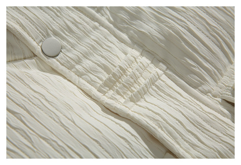 Close-up of an ivory jacket snap and gathered elastic detail against textured fabric.