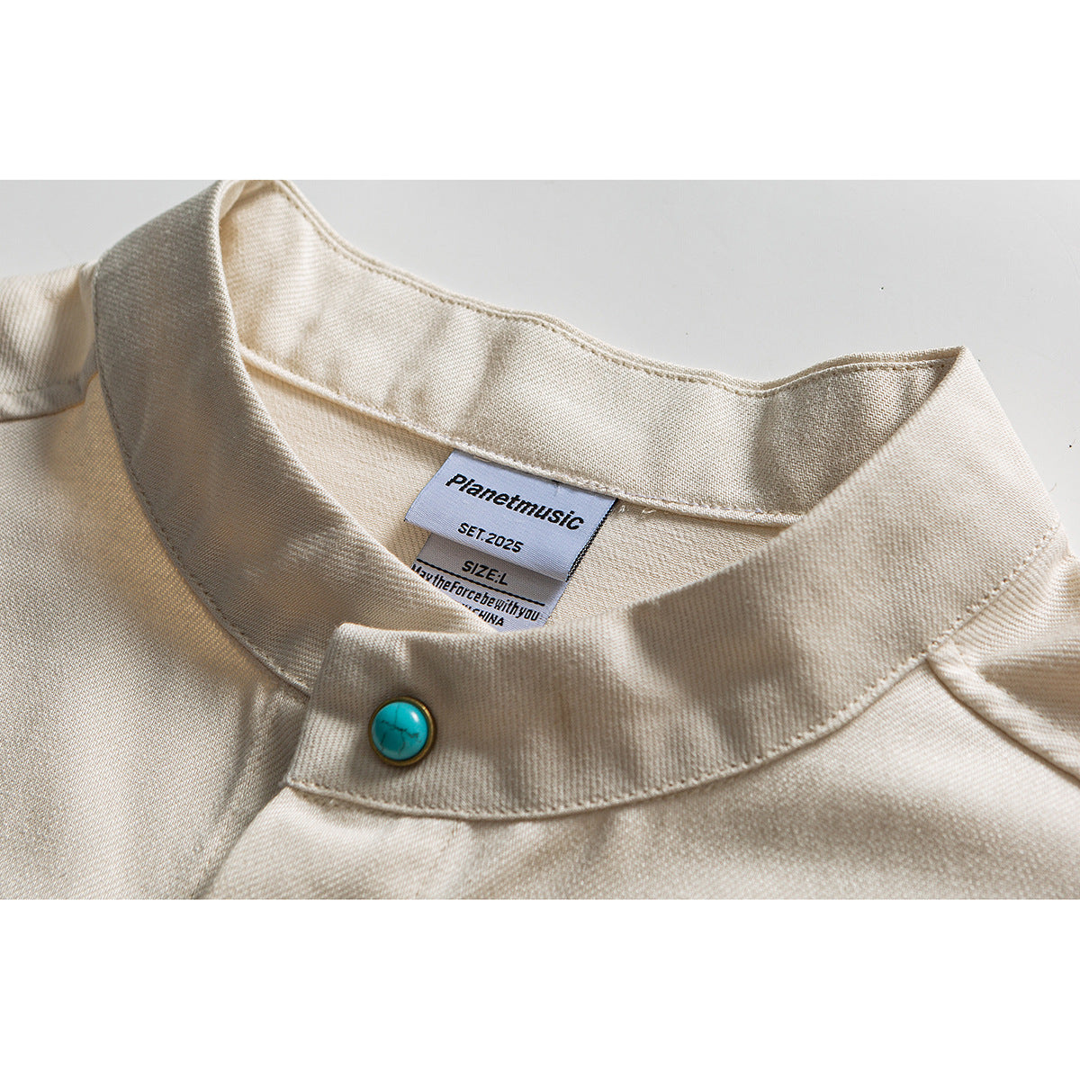 Close-up of a cream shirt's stand collar and turquoise button, with its sewn neck label visible.