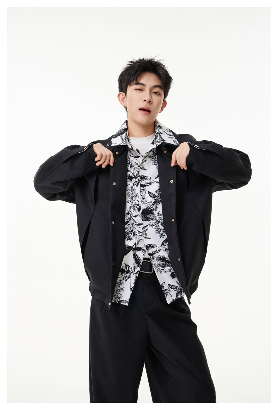 Man wearing an open black jacket over a black-and-white botanical print shirt, showing the jacket's snap front.