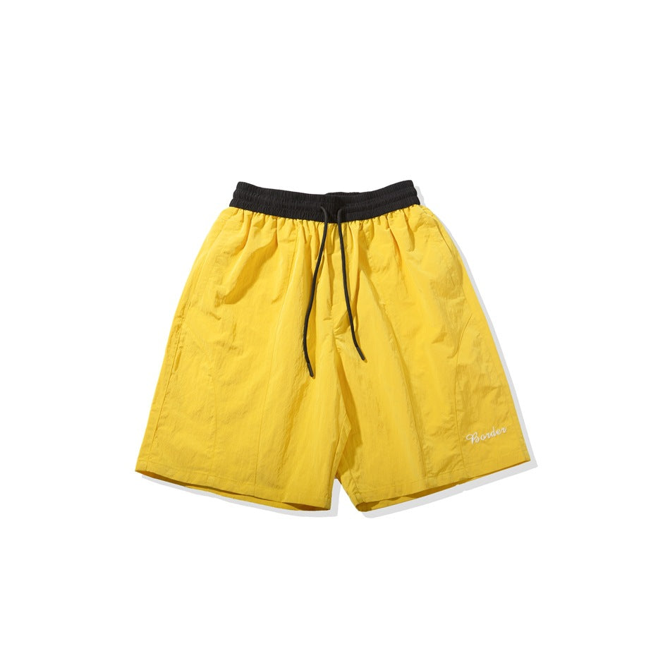 Front view of yellow shorts with a black elastic waistband, black drawstring, and small white script embroidery.