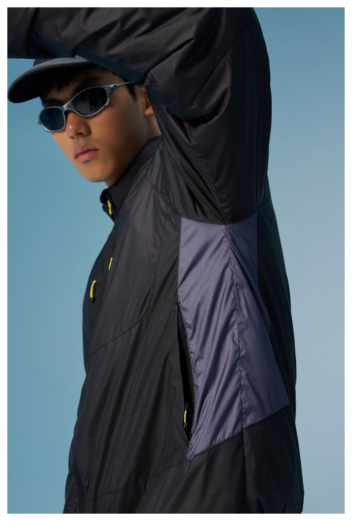 Side view of a black jacket with a purple underarm panel and a yellow-pull zip opening.