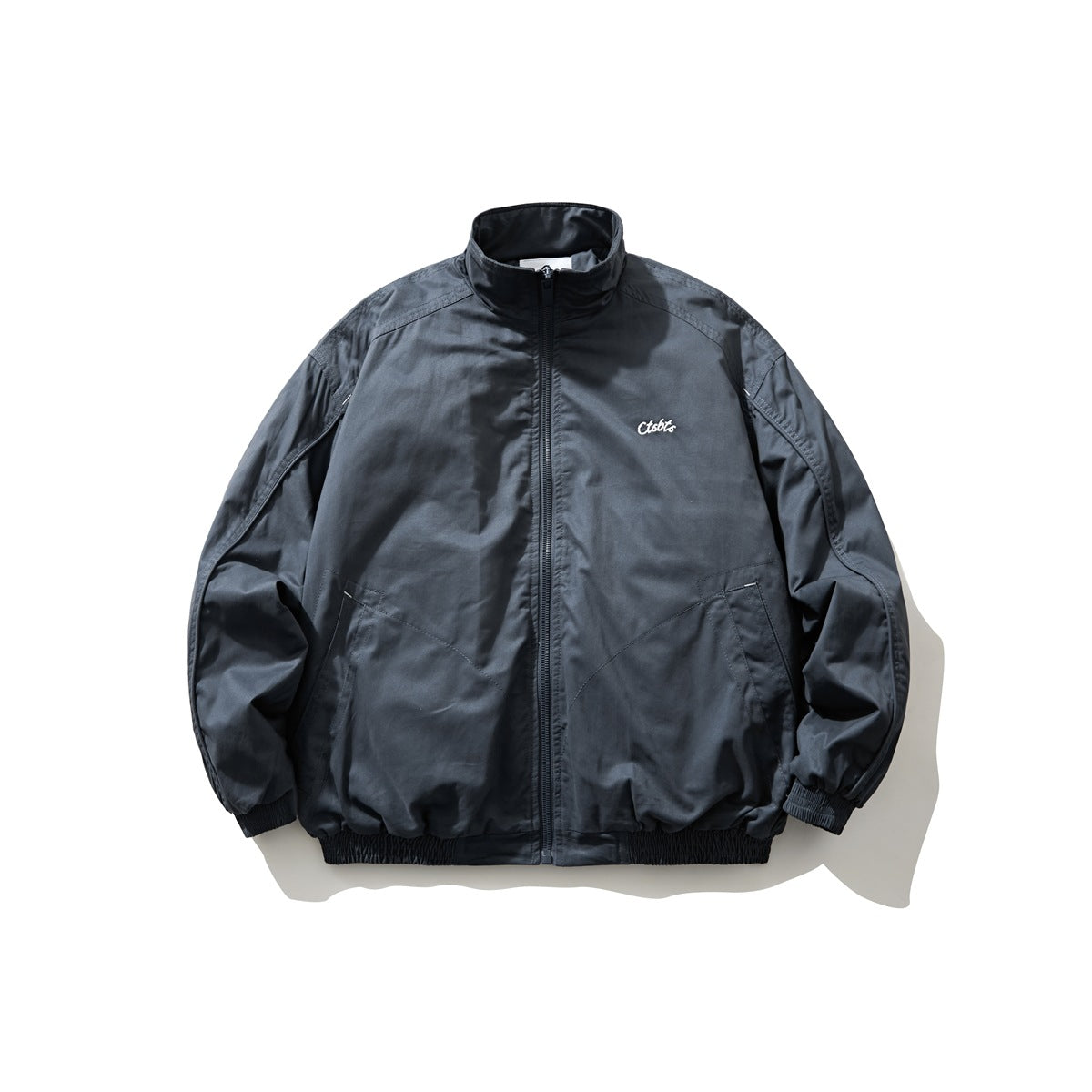 Blue-gray zip-up stand-collar jacket with white script chest embroidery, slanted pockets and elastic cuffs and hem, flat lay