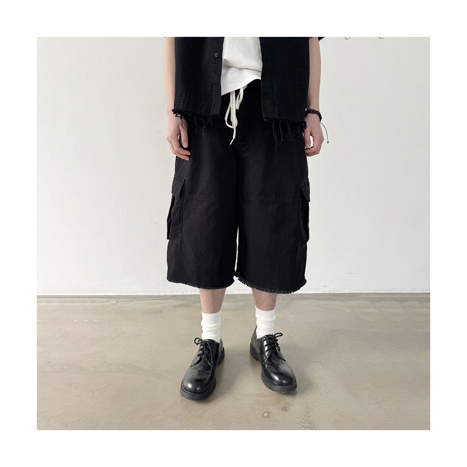 Person wearing black cargo shorts with side flap pockets and frayed hems, with a black shirt, white socks and black shoes