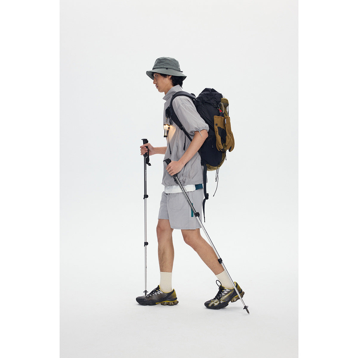 Side view of a model wearing a light gray short-sleeve zip jacket and matching shorts with a hiking backpack.
