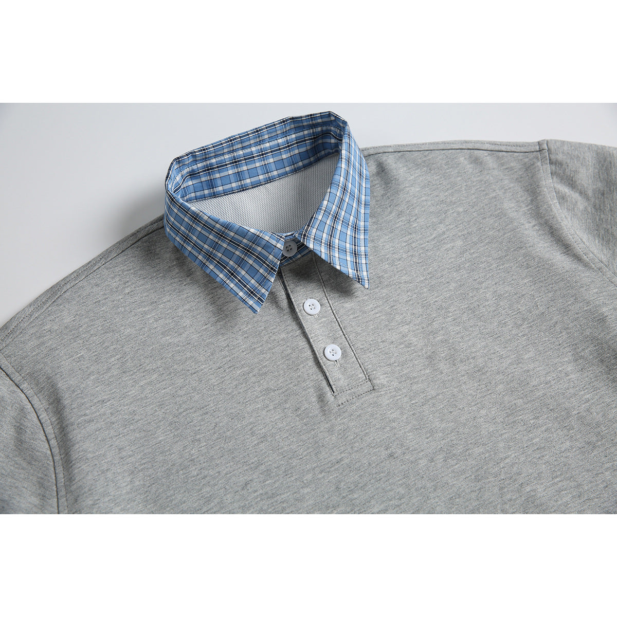 Close-up of a heather gray short-sleeve polo layered over a blue plaid shirt, showing its pointed plaid collar and button