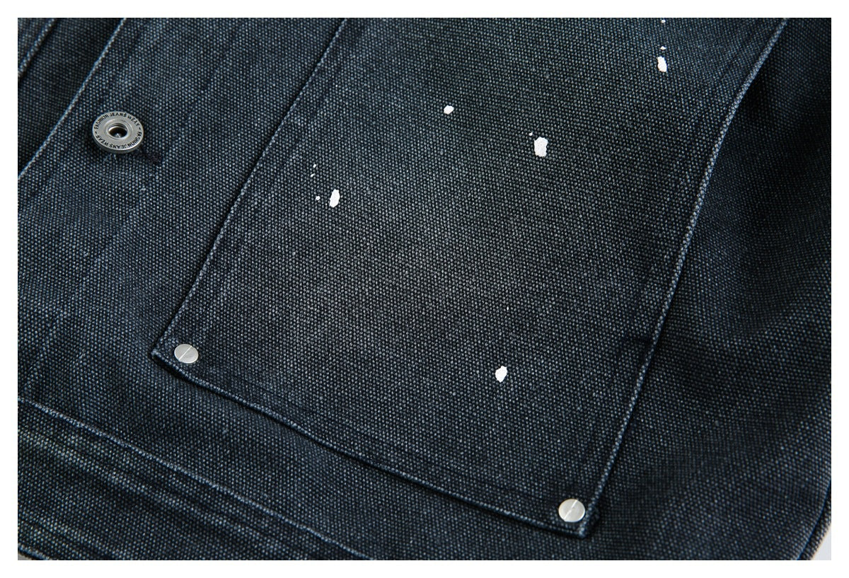Close-up of a large snap pocket on dark textured denim, with scattered white paint flecks.