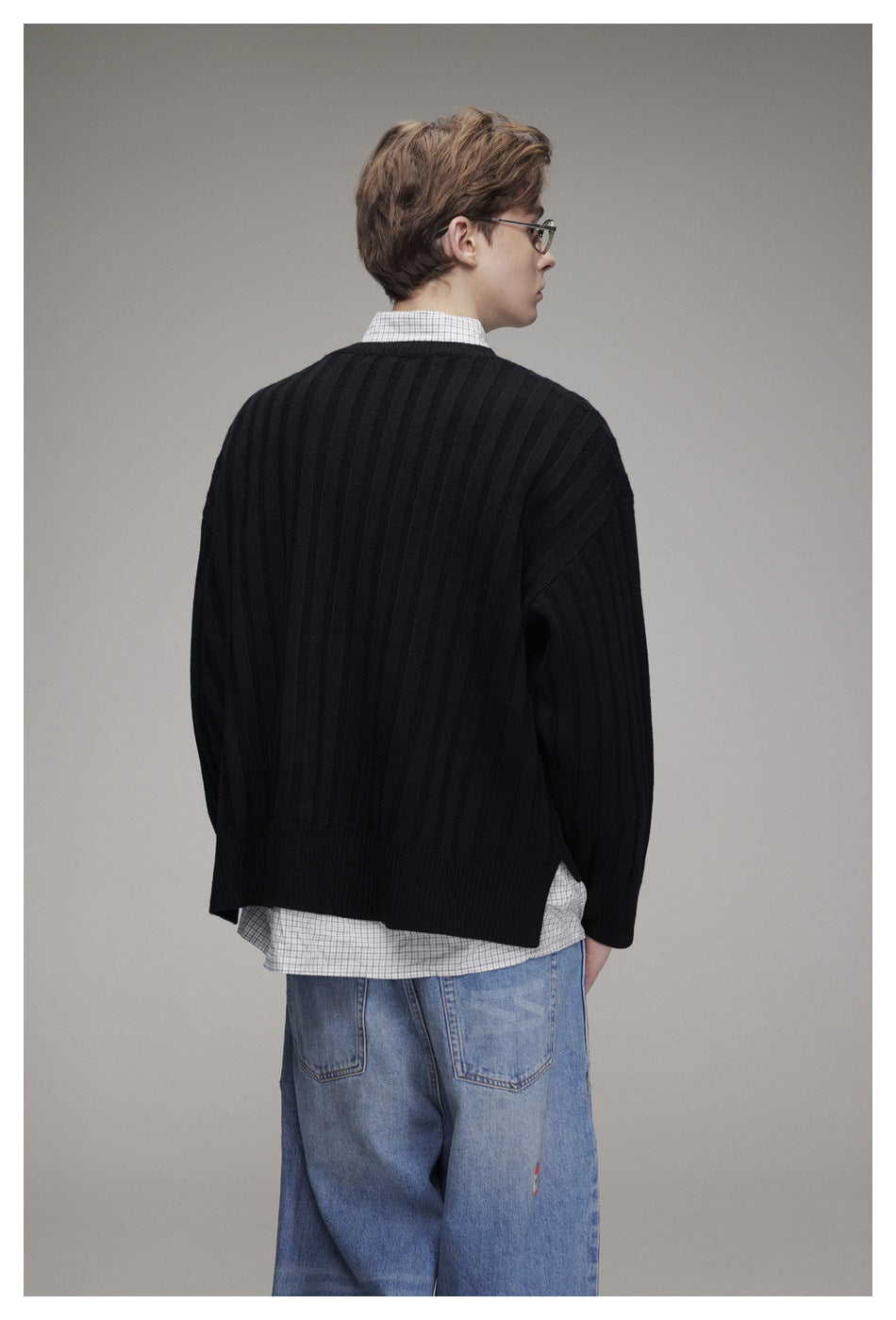 Rear view of a model wearing a black ribbed sweater over a checked shirt and loose blue jeans.