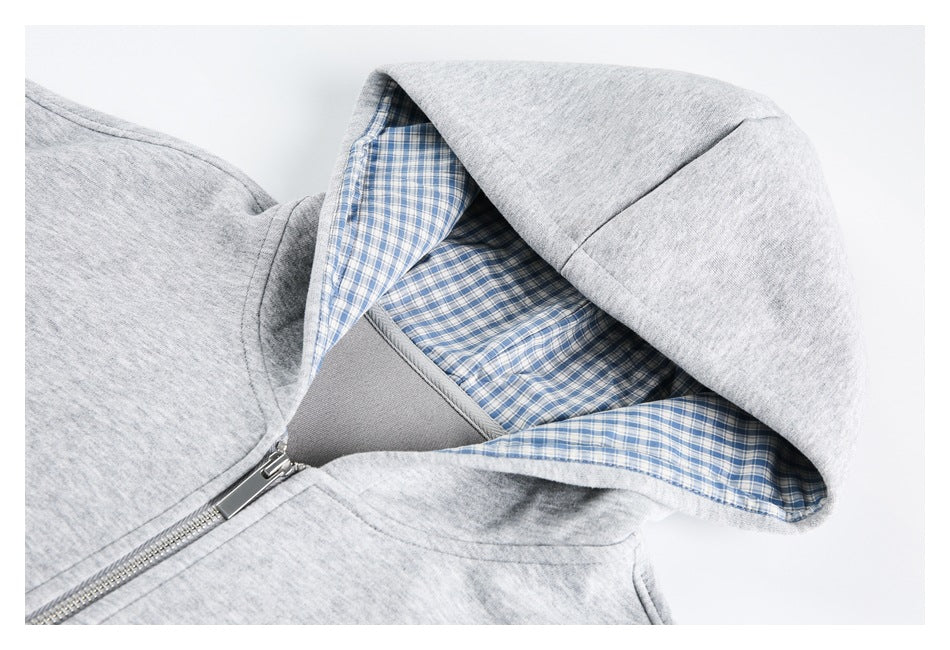 Close-up of a light gray zip-up hoodie showing its hood lined with blue-and-white plaid fabric.