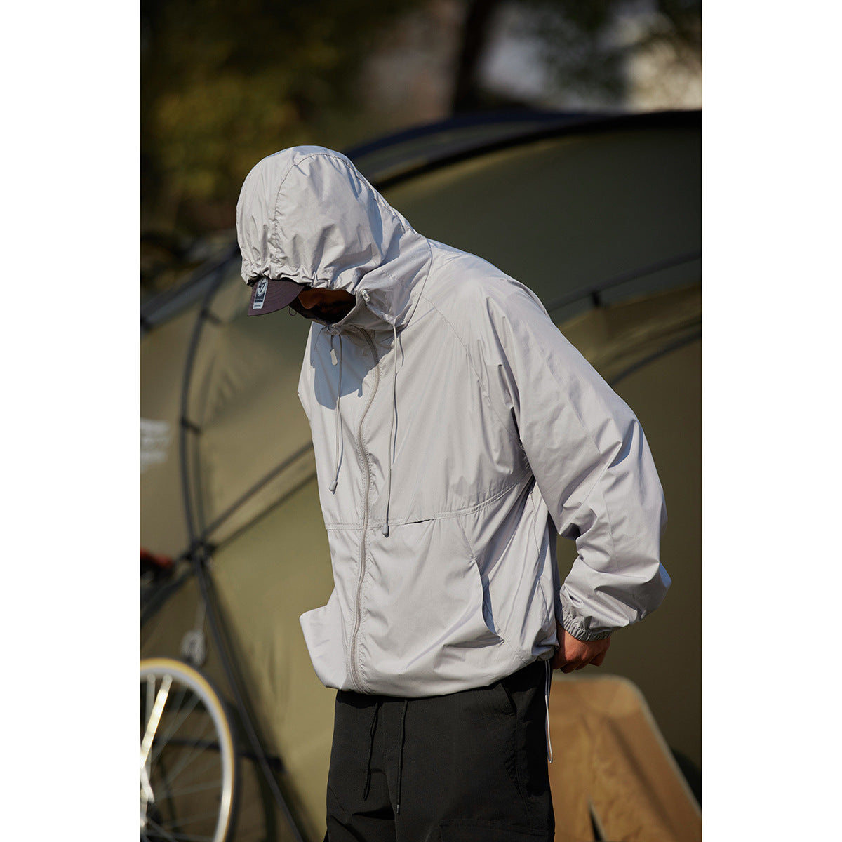 Closer view of a model wearing a light gray hooded jacket with drawcords, a front zipper and elastic cuffs.