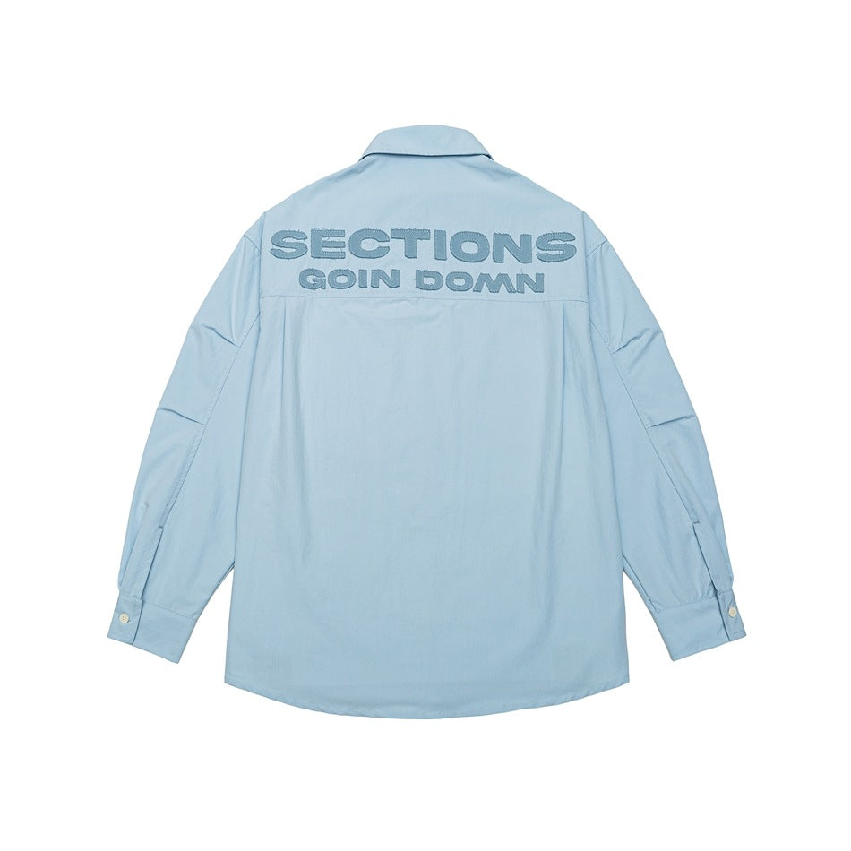 Light blue long-sleeve shirt, back view, with tonal embroidered lettering across the upper back and pleated sleeves