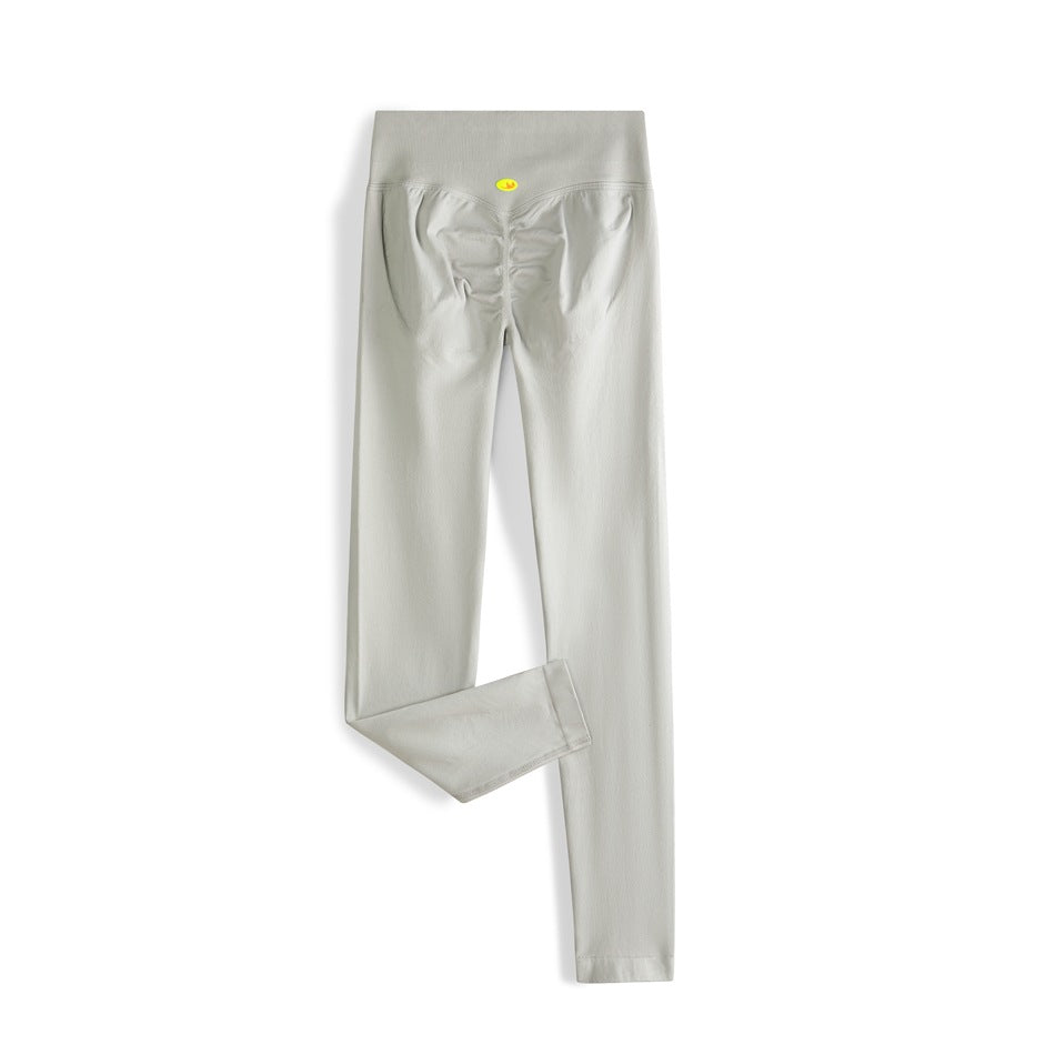 Flat lay of light gray leggings viewed from the back, with a wide waistband and gathered ruching at the seat.