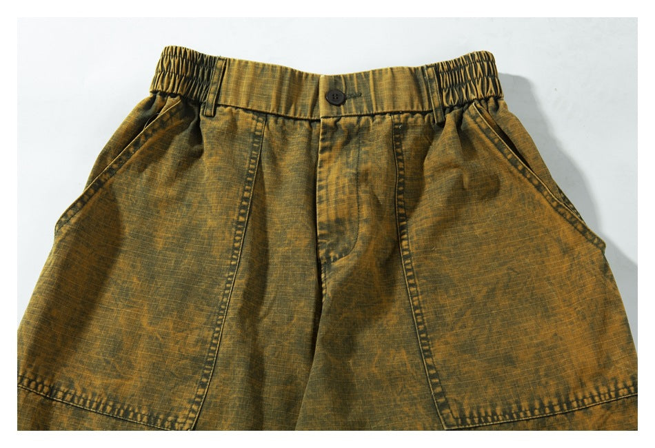 Front waist close-up of ochre-brown trousers with a button, elasticated sides, slanted pockets and panel seams.