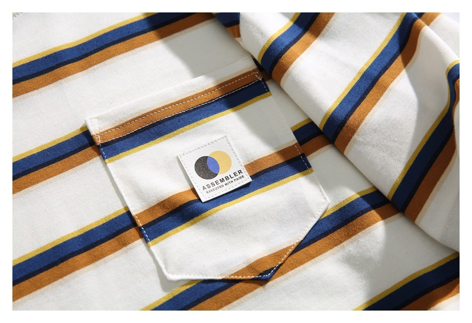 Close-up of the cream T-shirt’s striped chest pocket and sewn logo patch.