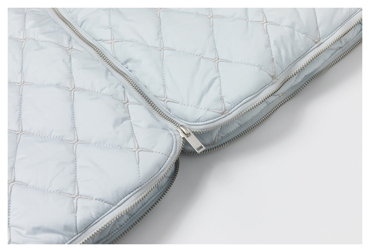 Close-up of overlapping silver zippers and quilted panels on a pale blue garment.