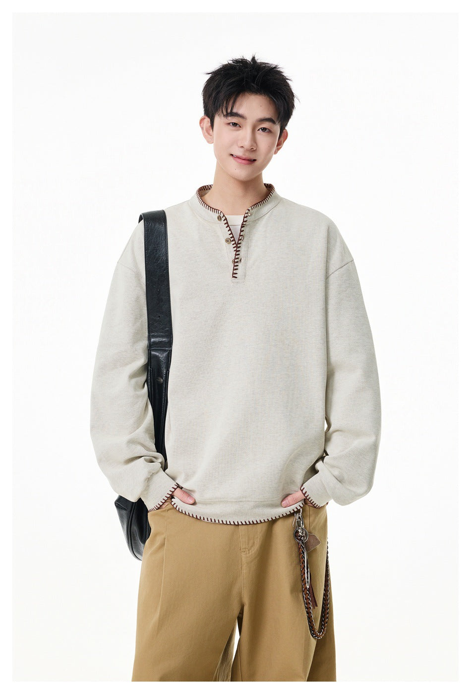 Man wearing a cream pullover with a short button placket and dark contrast stitching, shown from the front.