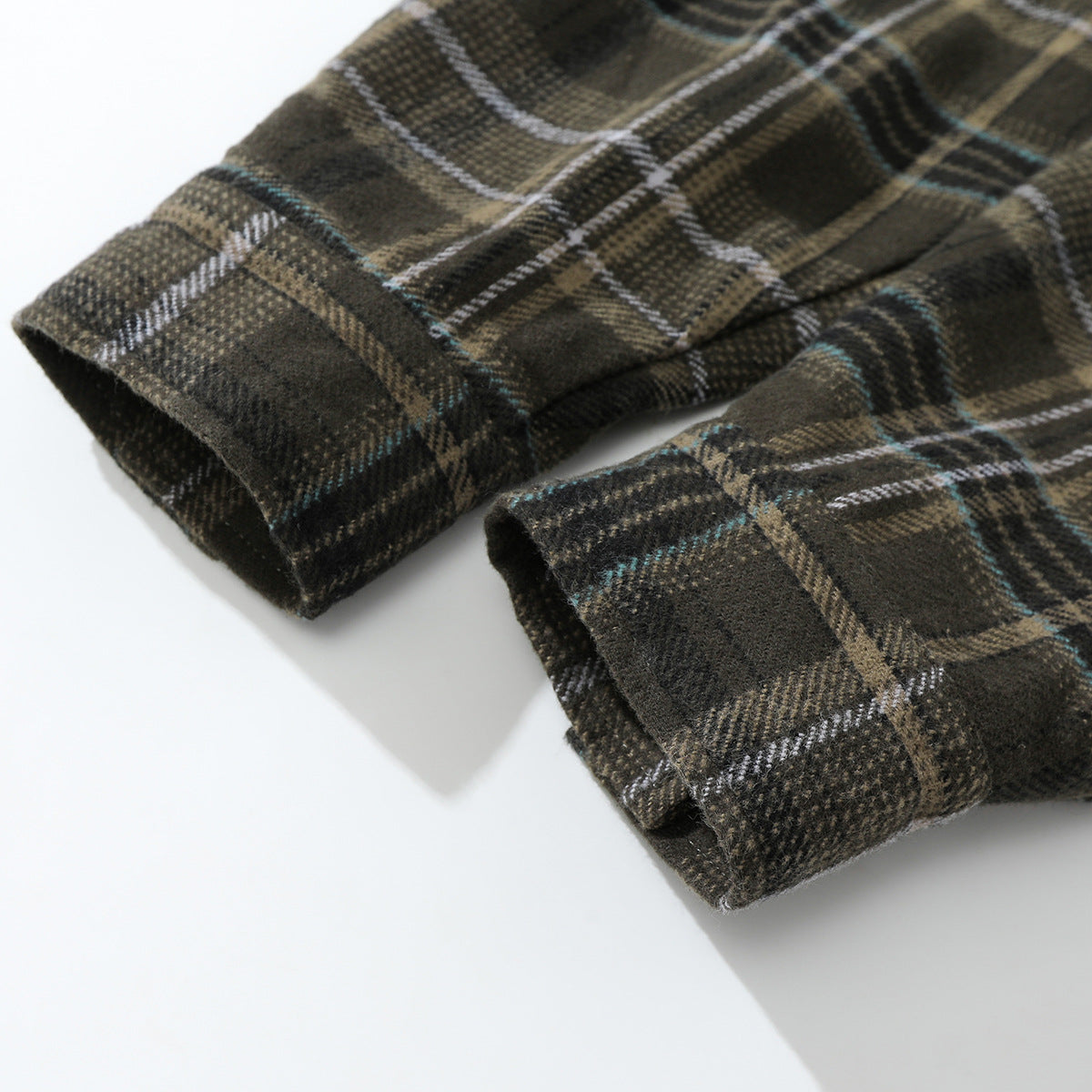 Close-up of two folded cuffs on a dark plaid shirt with tan, white, and teal lines.