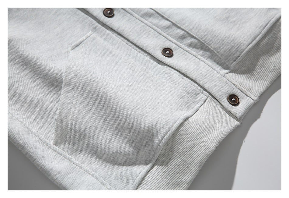 Close-up of a light gray sweatshirt with a patch pocket, ribbed trim, and dark buttons.