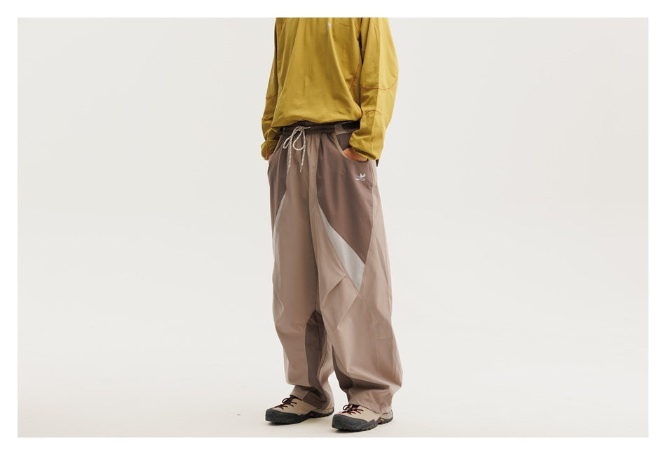 Model wearing loose taupe pants with a drawstring waist, side pockets and pale angular contrast panels.