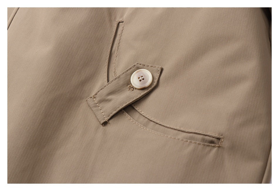Close-up of beige garment fabric with a buttoned tab over a curved welt pocket.