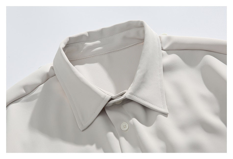 Close-up of the pointed collar and top button of an off-white button-up shirt.