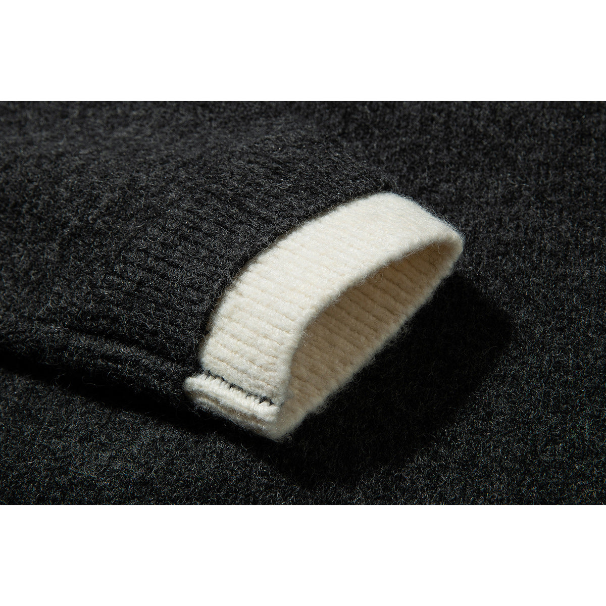 Close-up of a charcoal knit cardigan sleeve with a wide folded cream cuff.