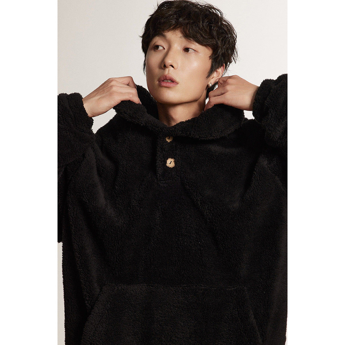 Close view of a model holding the wide collar of a black plush pullover with wooden-look buttons.