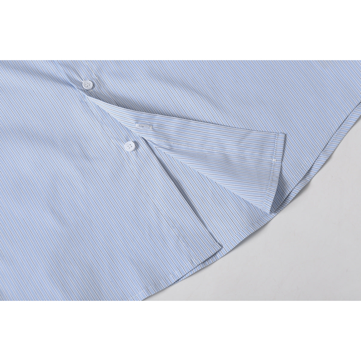 Close-up of the light blue striped shirt's pocket seam, buttons, and curved hem.