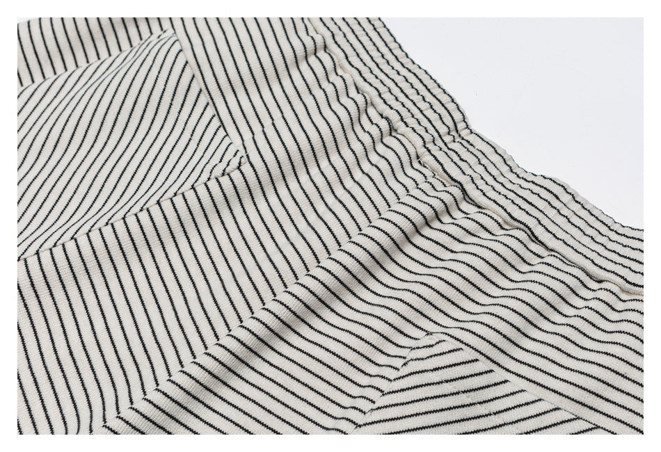 Close-up of cream pants with narrow black stripes, highlighting the elastic waistband and pocket seam.