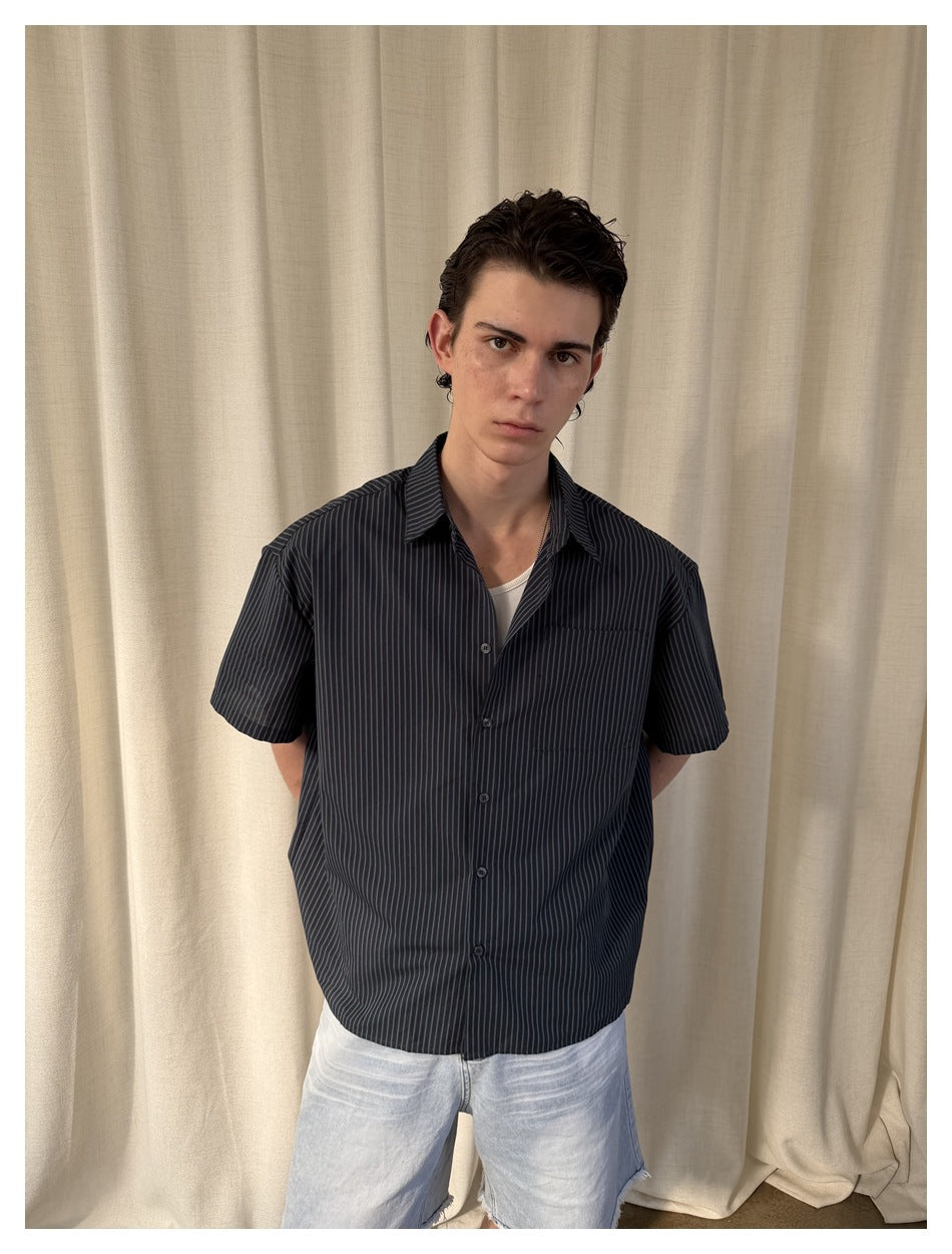 Closer front view of a model in a black pinstriped short-sleeve button-up shirt with a chest pocket.