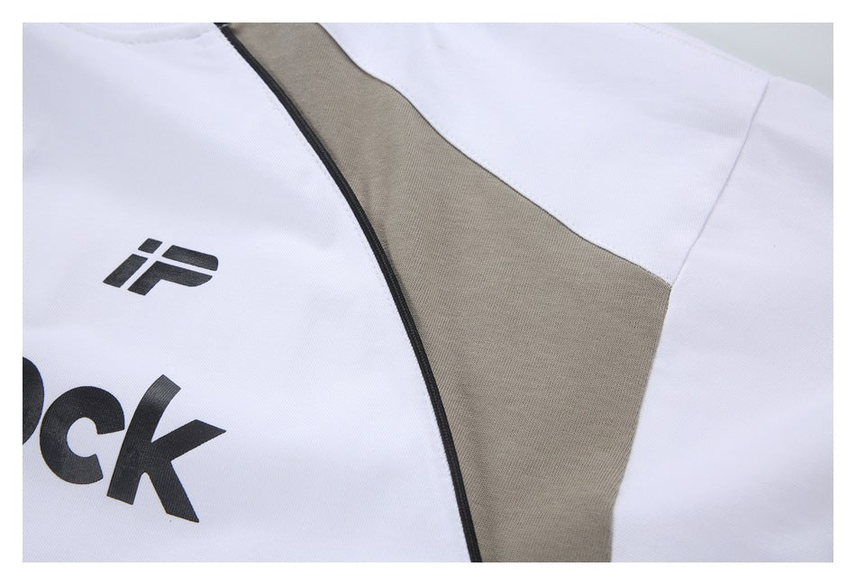 Close-up of a white garment with a taupe panel, black piping, and part of a black logo and lettering.