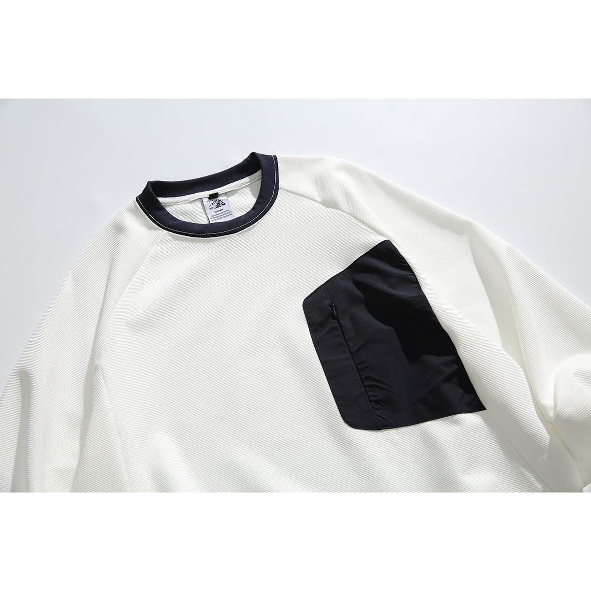 Close front view of an off-white long-sleeve crewneck with a dark navy collar and large navy chest pocket.