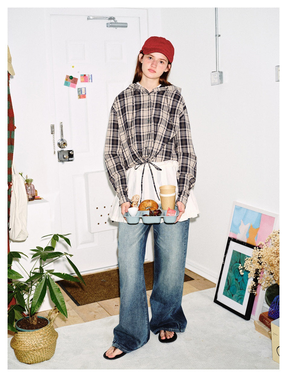 Full-length front view of a model wearing a gray plaid hooded button-up, white pleated layer, and wide-leg jeans.