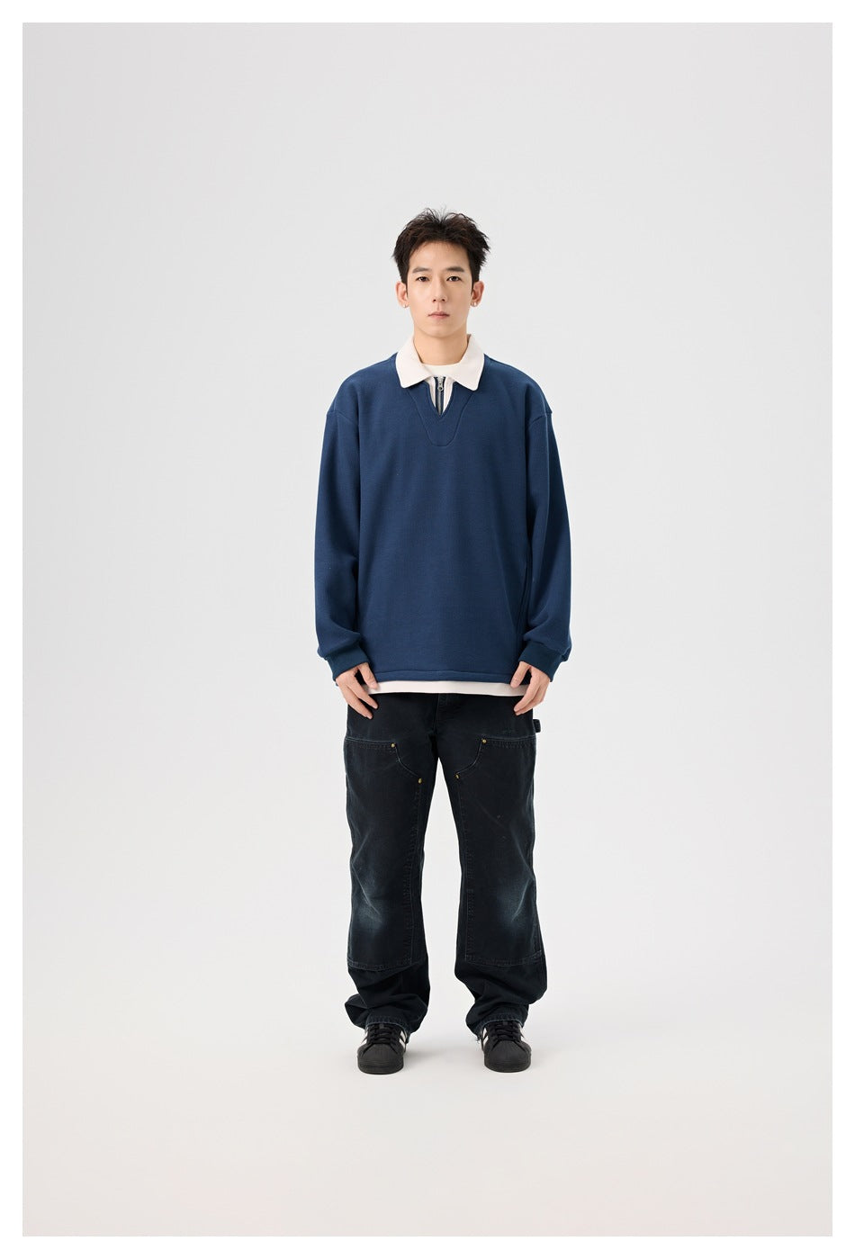 Model wearing navy pullover sweatshirt with cream polo collar and quarter-zip, over dark jeans, standing front view