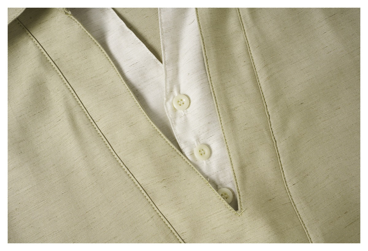 Close-up of a pale olive-beige garment's V-shaped button placket and stitched panels.
