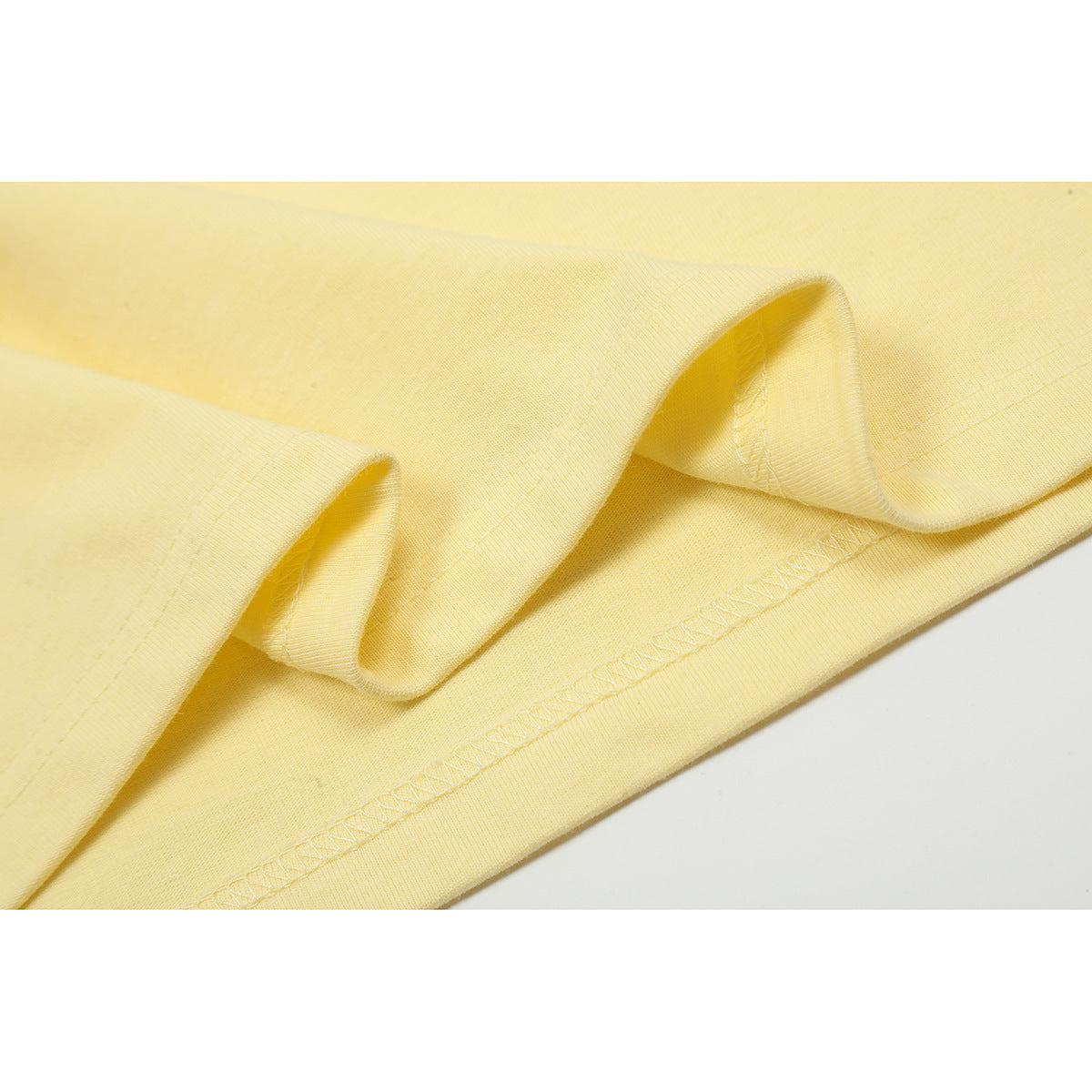 Close-up of the pale yellow T-shirt's folded fabric and stitched bottom hem.