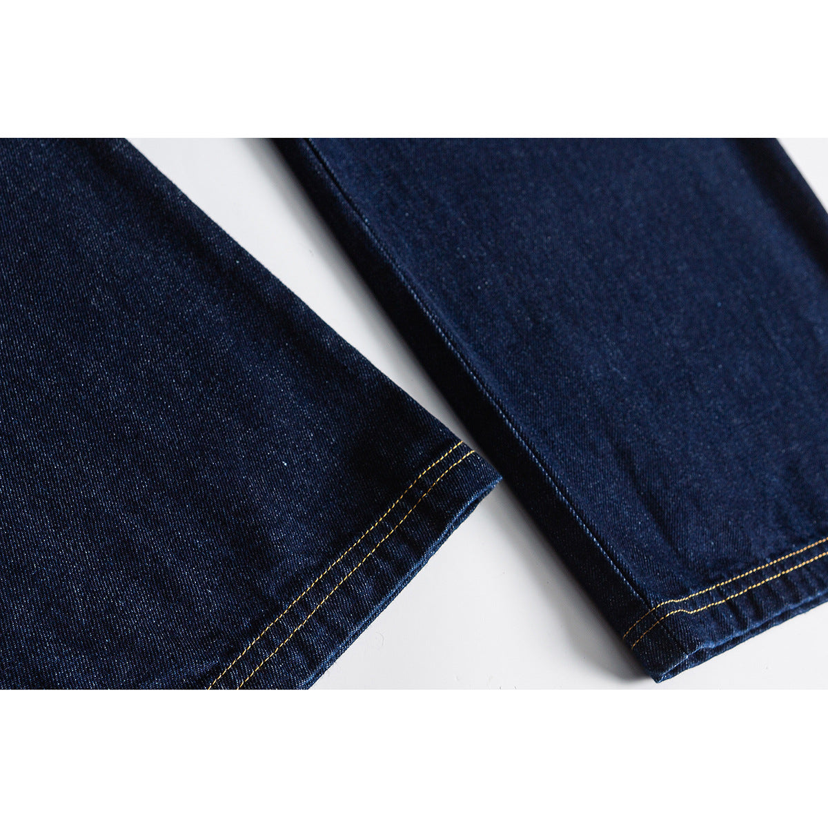 Close-up of dark indigo jean legs with straight hems and contrasting golden-brown stitching.