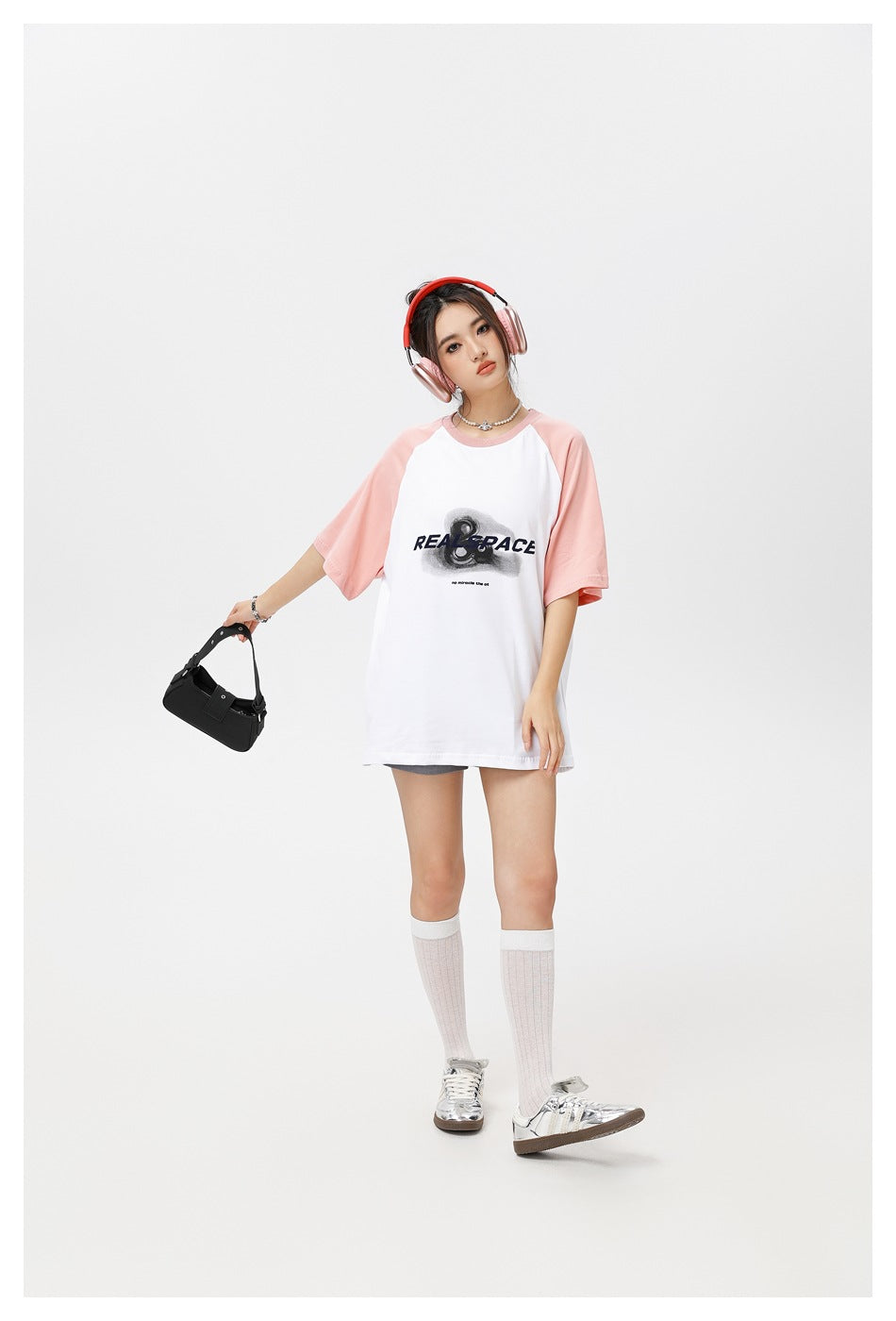 Model wearing a white oversized raglan T-shirt with pale pink sleeves and a black chest graphic, with headphones and a small