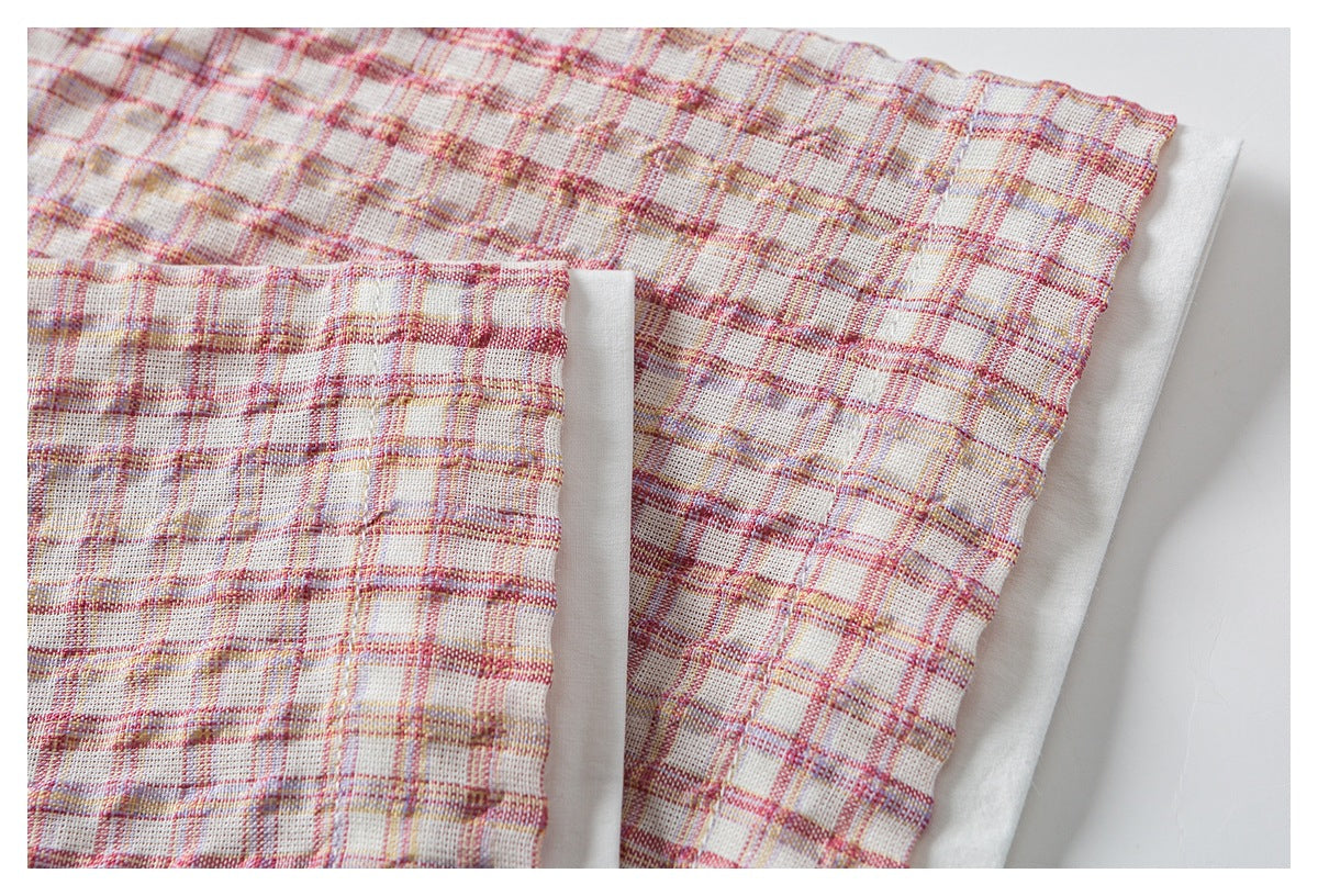 Close-up of the pink plaid garment's gathered edge and folded seam against a white surface.