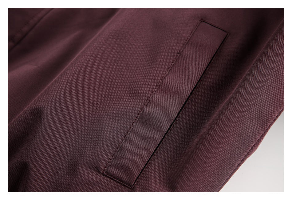 Close-up of a long, narrow stitched pocket on burgundy textured fabric.