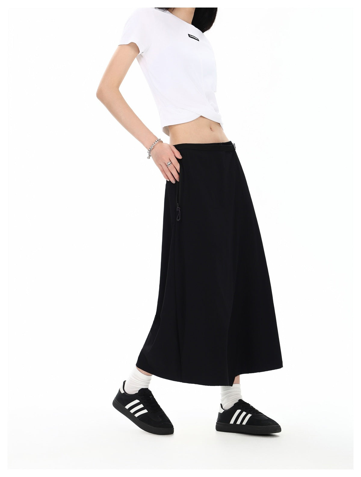 Angled side view of a model wearing a black ankle-length wrap skirt with a side zipper and a white cropped T-shirt.