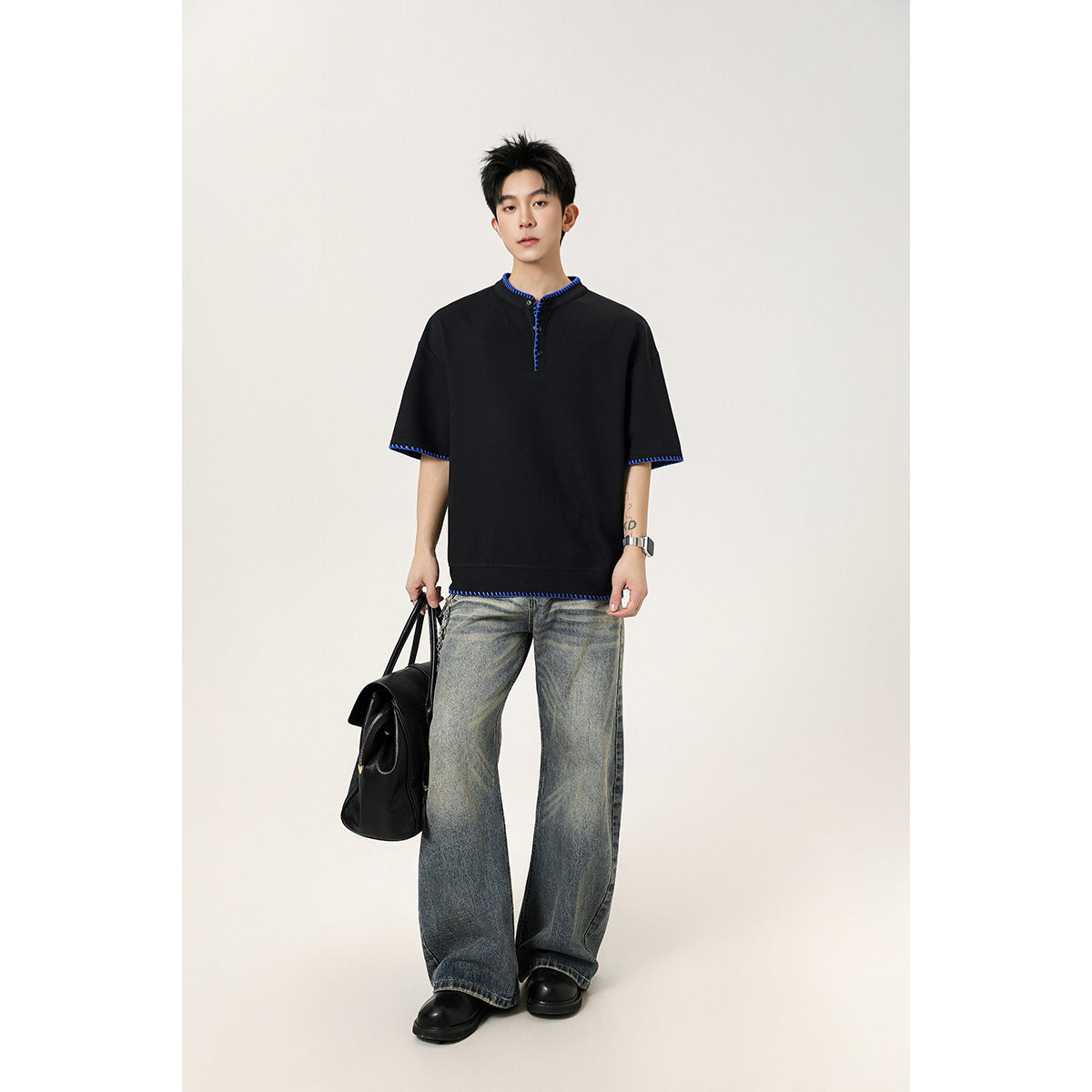 Model wearing a black short-sleeve henley with bright blue contrast stitching and faded wide-leg jeans.