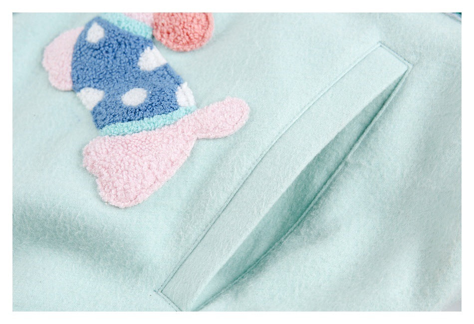 Close-up of a pink-and-blue animal appliqué beside a stitched pocket on a pale mint coat.