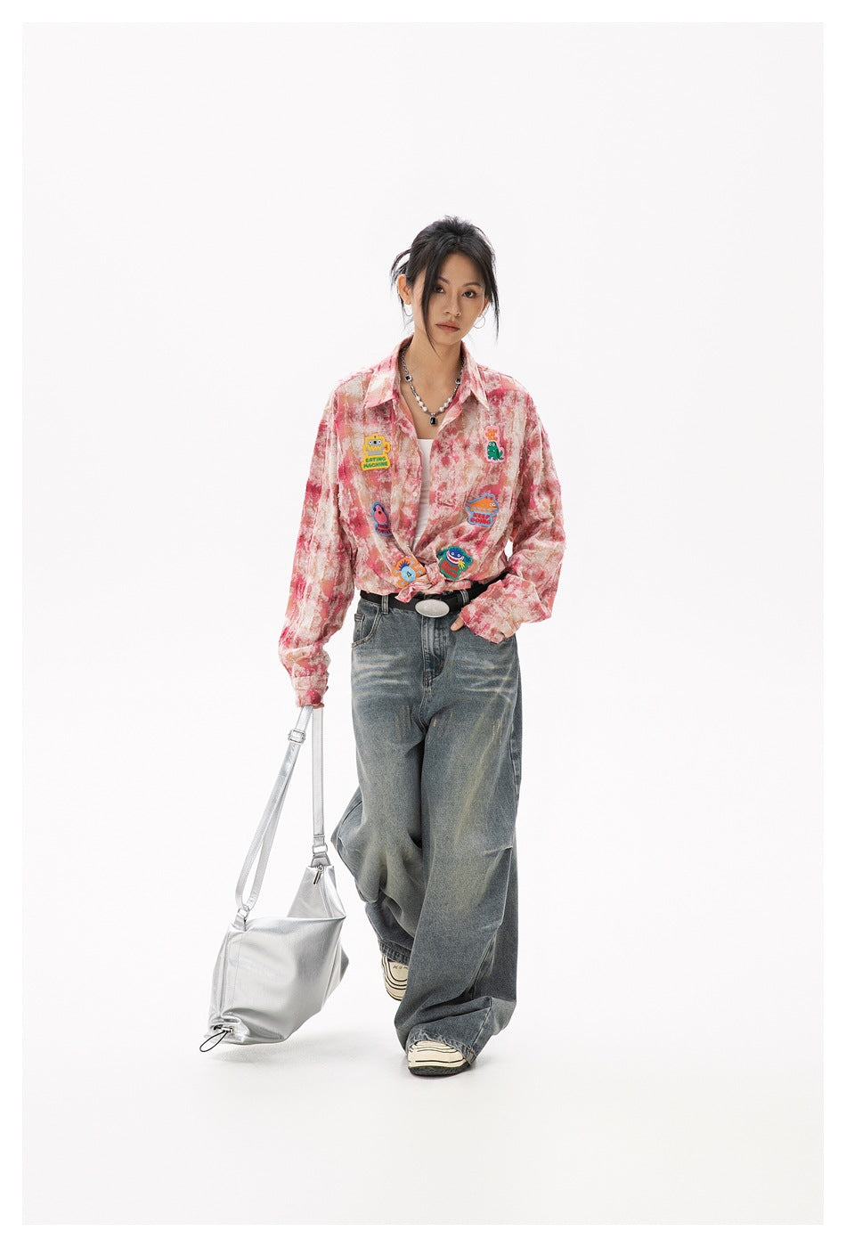 Model walking in a pink-and-cream patterned shirt with colorful patches, tied at the waist, and wide-leg jeans.