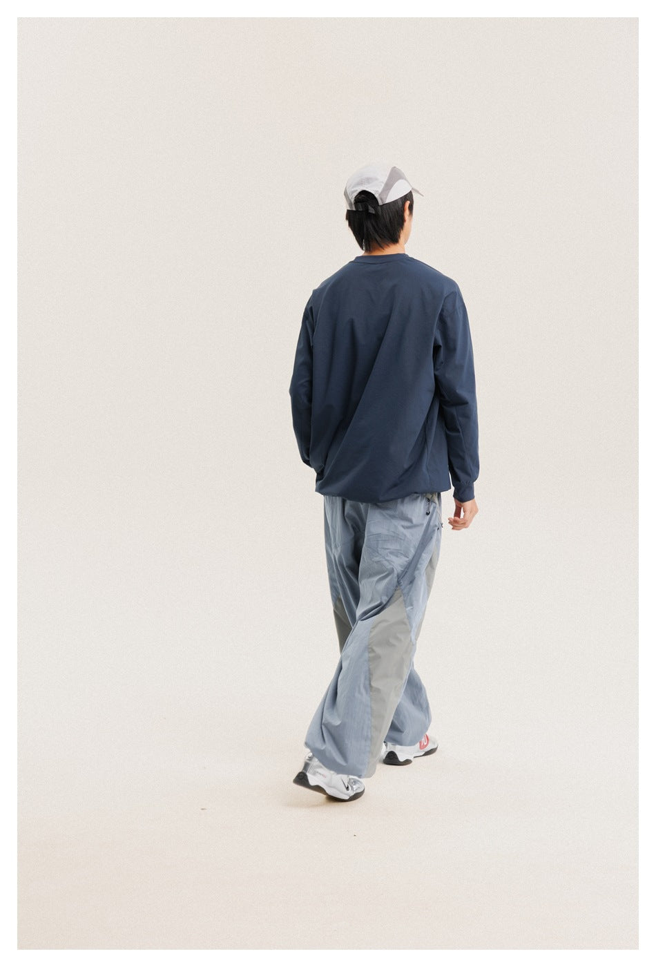 Rear view of a model wearing a navy long-sleeve shirt and pale blue wide-leg pants with contrasting side panels.