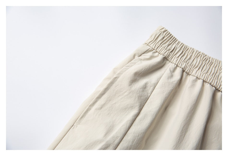 Close-up of cream shorts showing the gathered elastic waistband and stitched fabric panels.
