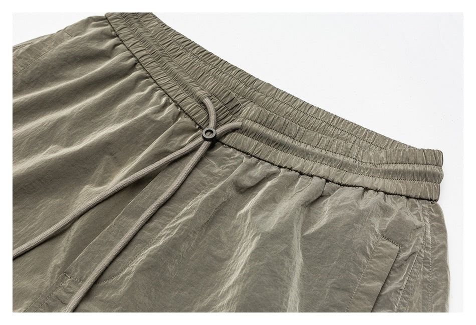 Close-up of the olive-gray shorts' gathered waistband, adjustable drawcord and side pocket opening.