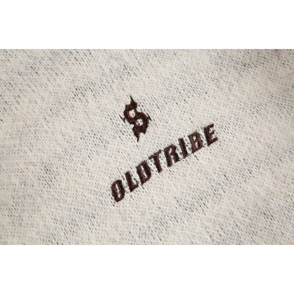 Close-up of dark embroidered lettering and emblem on ivory sweater knit.