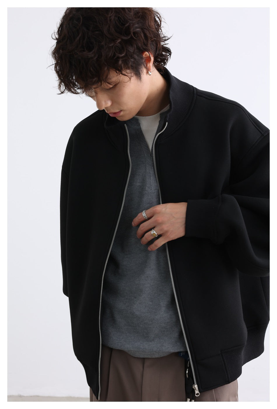 Close view of a model wearing an open black zip jacket with a ribbed stand collar and cuffs.