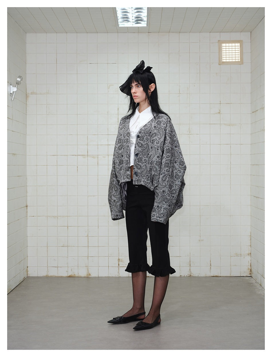 Model in the gray paisley oversized jacket with wide sleeves over a white shirt, three-quarter side view